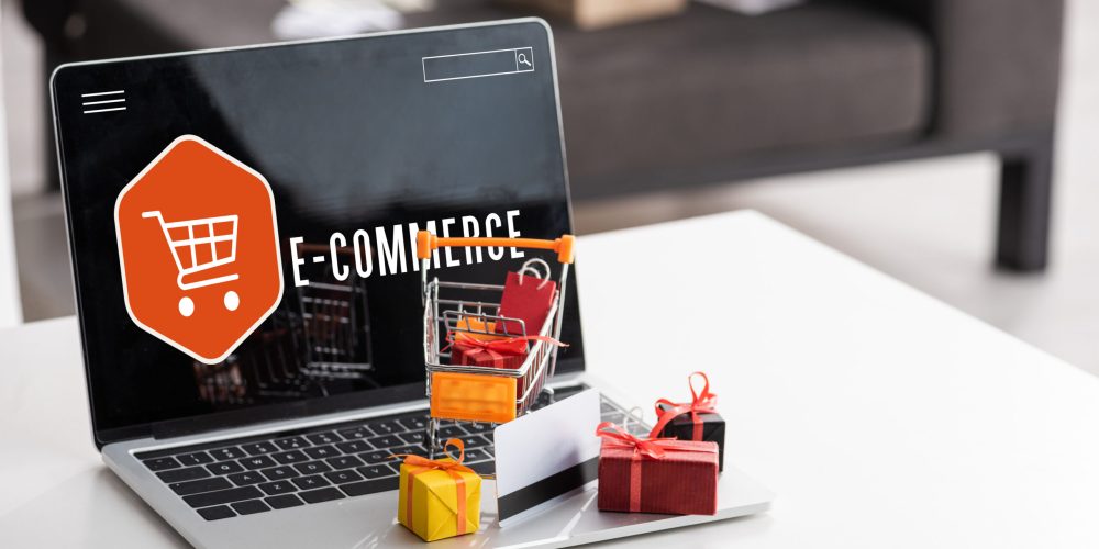 Toy gift boxes and credit card on laptop with e-commerce lettering on table